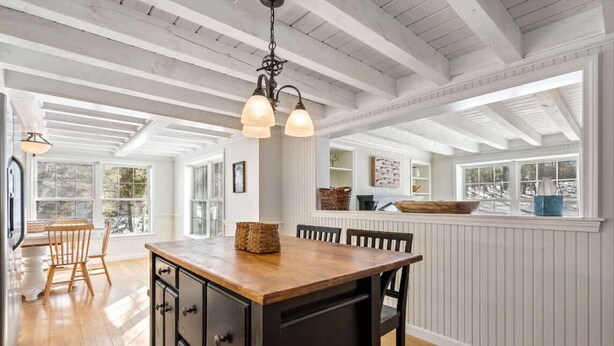 Una cocina amplia con una isla de madera, paredes blancas con paneles y ventanas grandes.