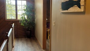A wooden interior hallway with a ceiling fan, a large window, and a potted plant.