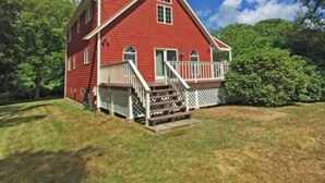 A red two-story house with a white porch and a small deck.