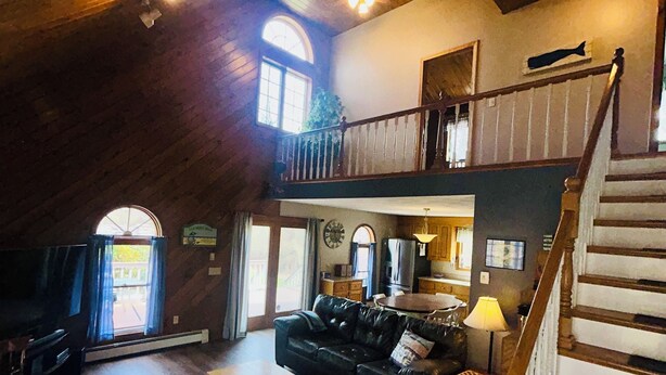 A spacious living room with a wooden ceiling, a staircase, and a dining area.