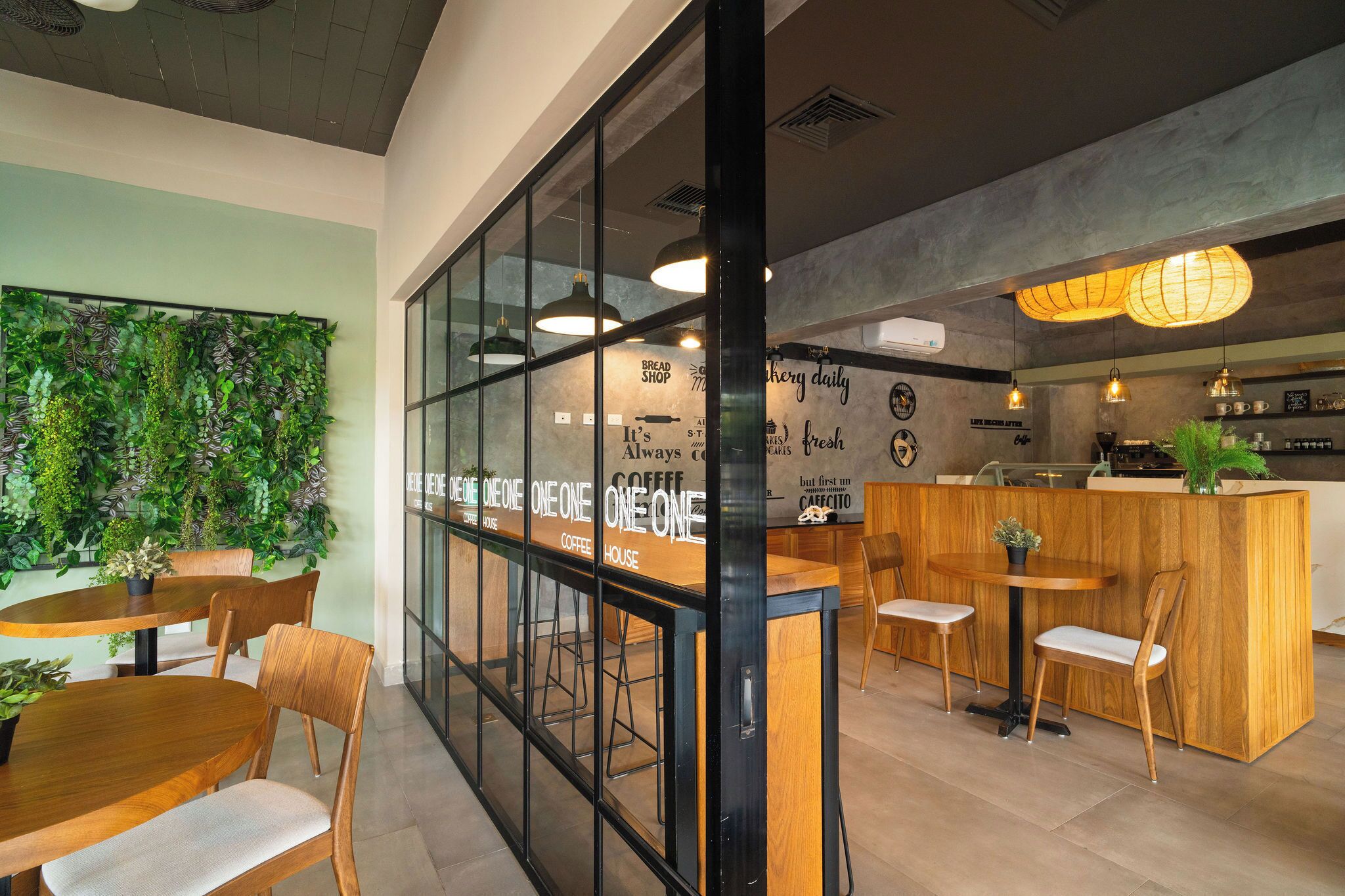 L’intérieur d’un café moderne, avec des tables et des chaises en bois, un mur végétal et un comptoir où se trouve une machine à café.