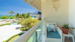 Un balcon donnant sur une plage, un élément décoratif suspendu, un canapé avec un coussin et une plante en pot.