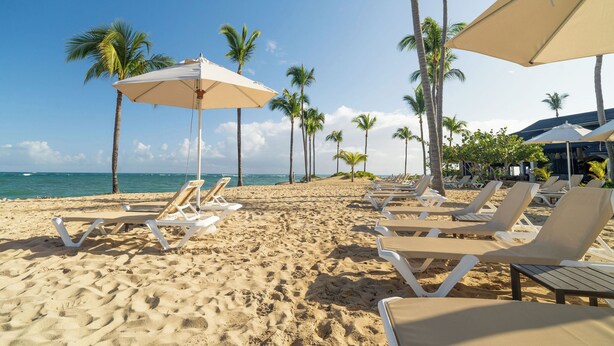 Une plage avec des transats et des parasols, des palmiers et un ciel dégagé.