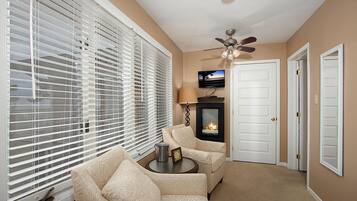 A living room with a fireplace, two sofas, a ceiling fan, and a TV mounted on the wall.