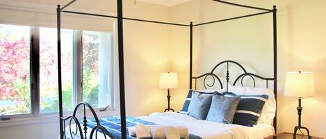 A four-poster bed with a canopy, two bedside lamps, and a wicker side table.