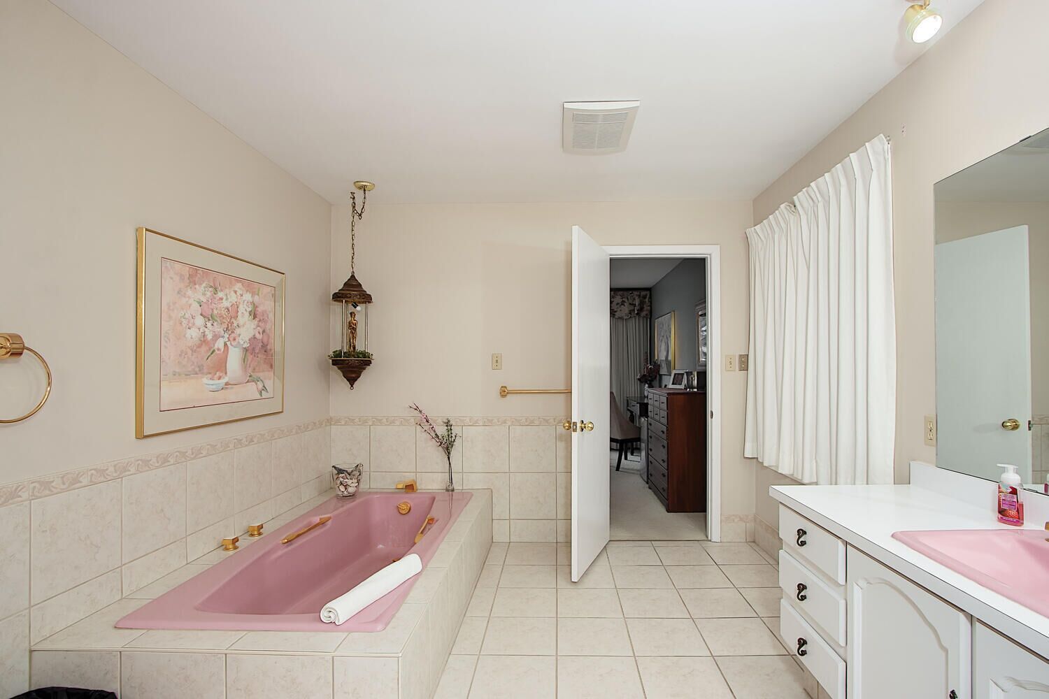 A bathroom with a large bathtub, a vanity with a mirror, and a door leading to another room.