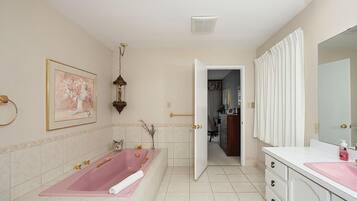 A bathroom with a large bathtub, a vanity with a mirror, and a door leading to another room.
