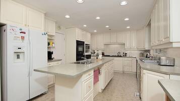 A modern kitchen with white cabinetry, a central island, and built-in appliances including a refrigerator, oven, and microwave.