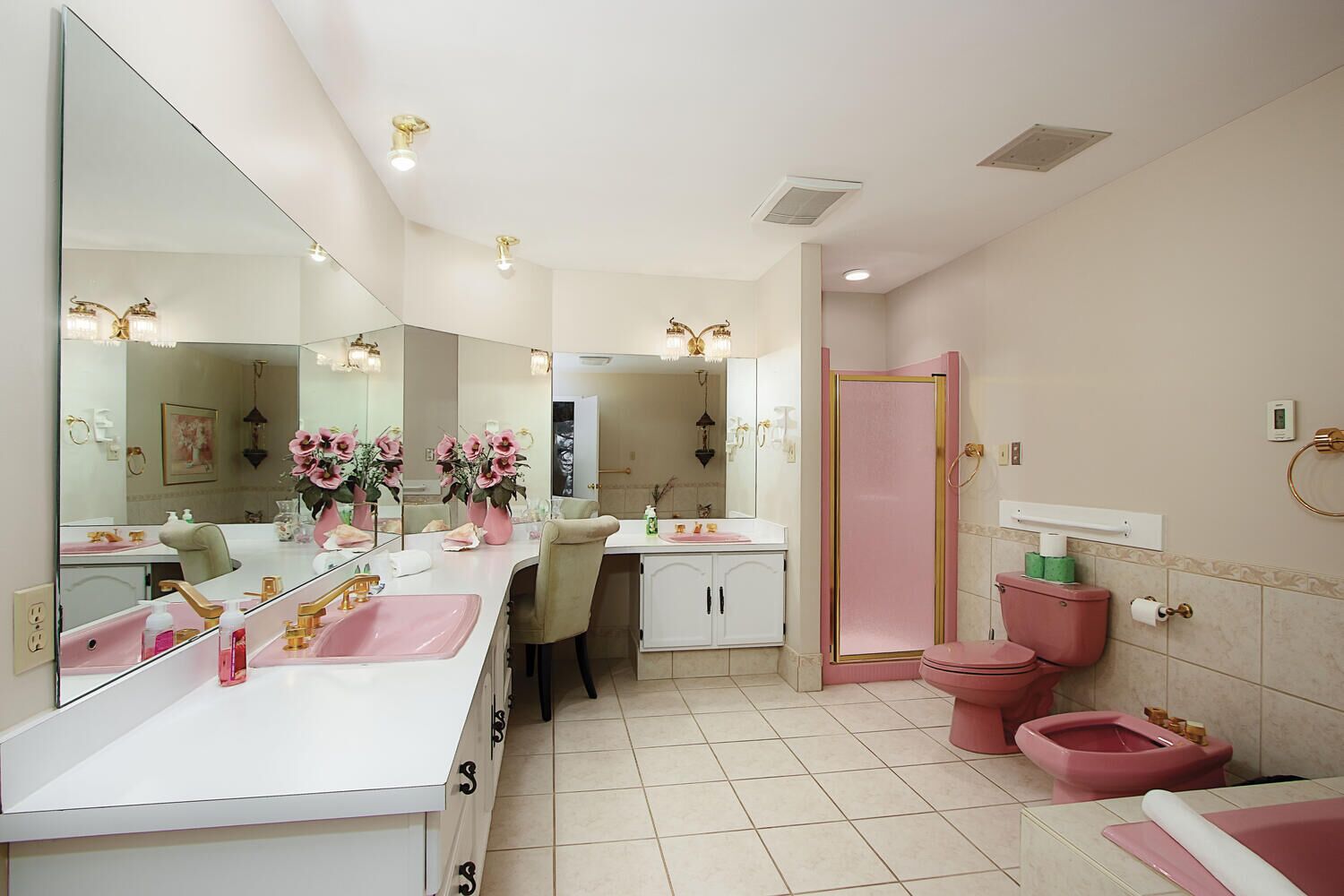 A modern bathroom with a large mirror, a vanity with a pink sink, and a separate toilet area.