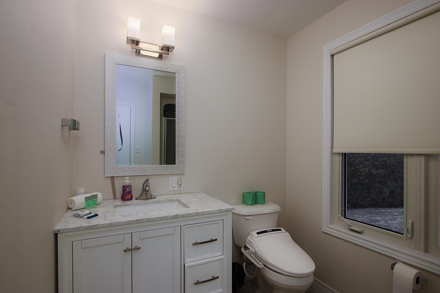 A bathroom with a white vanity, a toilet, and a window.