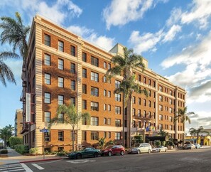 A multi-story hotel with a brick facade, multiple windows, and a parking lot with several cars. - San Diego | City Retreat | Fitness + Sun Deck (San Diego)