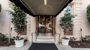 A hotel entrance with a covered entrance, steps leading to a glass door, and potted plants on either side. - San Diego | City Retreat | Fitness + Sun Deck (San Diego)