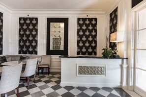 A room with a checkered floor, a seating area with a table and chairs, a decorative wall panel, and a reception desk with a plant. - San Diego | City Retreat | Fitness + Sun Deck (San Diego)