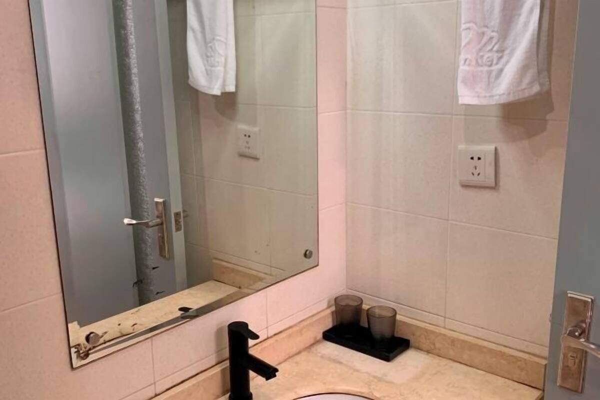 Un baño con un espejo grande, un lavabo y un perchero para toallas.