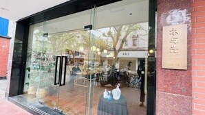 Una fachada con grandes ventanales de vidrio, un letrero y un muro de ladrillo.