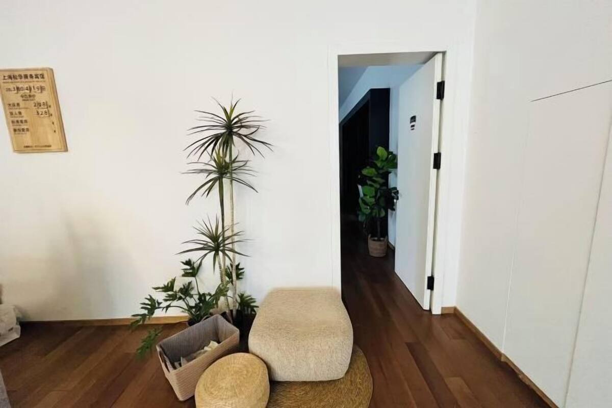 Una habitación con piso de madera, pared blanca, una planta, un banco y una puerta que da a otra habitación.