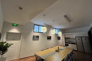 A modern kitchen with white cabinets, a long wooden table, and pendant lighting. - Songhua Business Hotel (Shanghai)