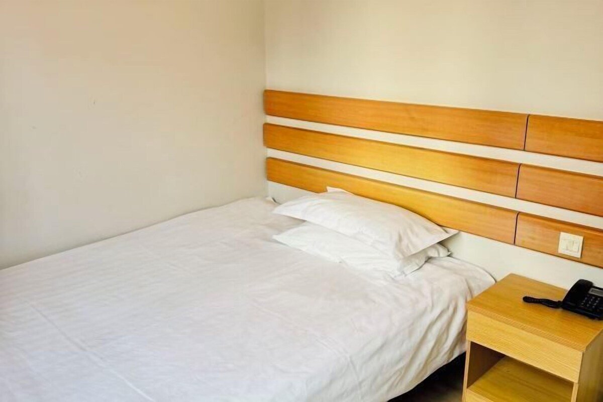 A single bed with a wooden headboard, white bedding, and a bedside table with a telephone.