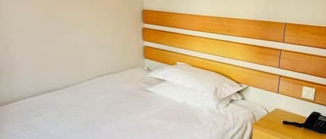 A single bed with a wooden headboard, white bedding, and a bedside table with a telephone.