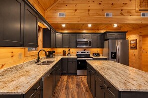 A modern kitchen with dark cabinets, granite countertops, stainless steel appliances, and wooden ceiling. - Waterfront Swimming + Pet Friendly | Hot tub (Cocke County)