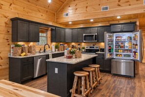 A modern kitchen with dark cabinets, stainless steel appliances, and a central island with stools. - Waterfront Swimming + Pet Friendly | Hot tub (Cocke County)