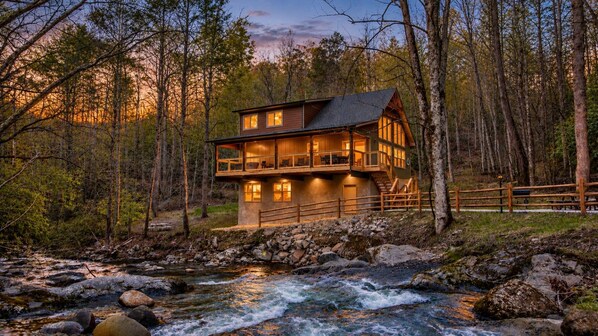 A cabin with a balcony, located near a river in a forested area. - Waterfront Swimming + Pet Friendly | Hot tub (Cocke County)