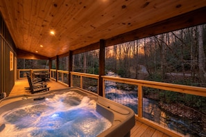 A hot tub on a wooden deck with a view of a forest and a river. - Waterfront Swimming + Pet Friendly | Hot tub (Cocke County)
