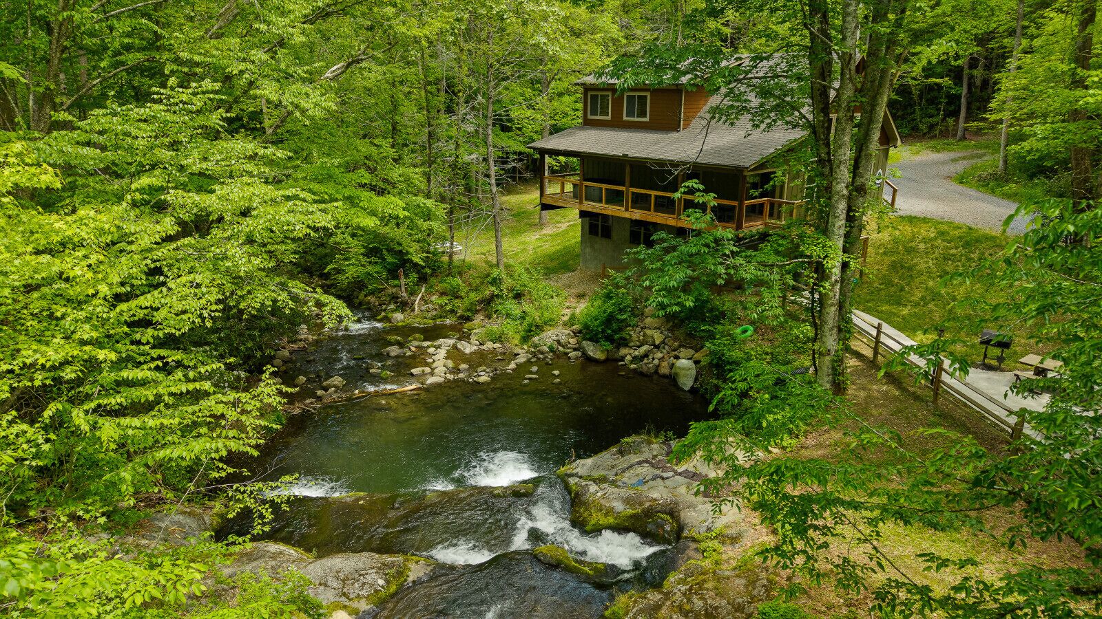 Une cabane dotée d’une terrasse donnant sur un ruisseau, entourée d’une forêt dense.