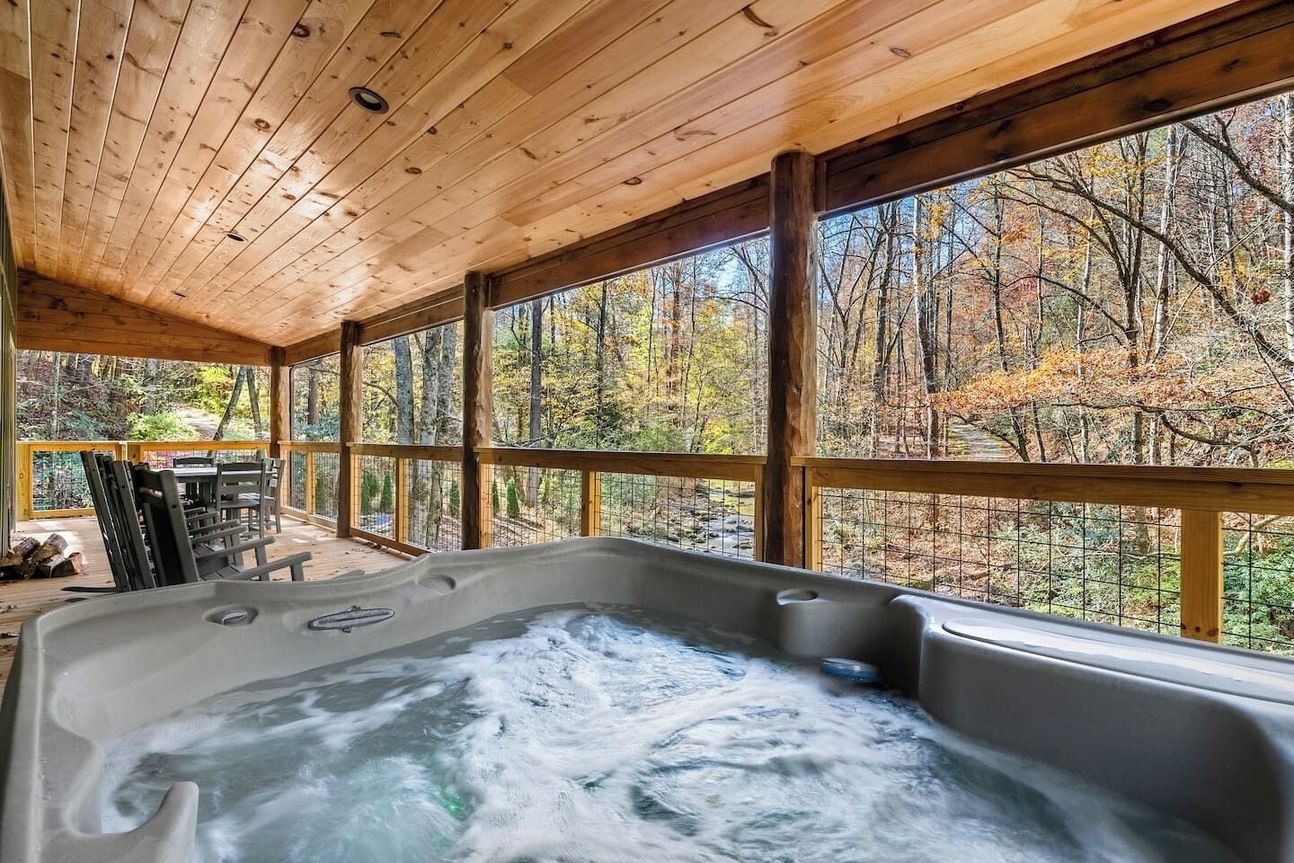 Une cabane en bois dotée d’un bain à remous, de grandes fenêtres et offrant une vue sur les arbres aux couleurs automnales.
