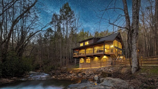 Eine Hütte mit Balkon, ein Fluss im Vordergrund und ein Sternenhimmel.
