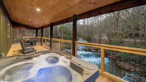 Eine Holzterrasse mit Whirlpool, mit Blick auf Fluss und Wald.