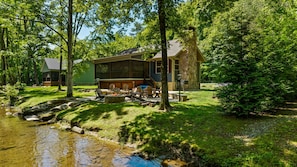 Une cabane avec un foyer extérieur, des sièges pour se détendre en plein air et un ruisseau à proximité.