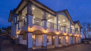 A large, two-story house with a balcony, multiple garage doors, and outdoor lighting.