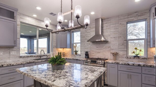 A modern kitchen with granite countertops, a central island, a stainless steel range hood, and a large window providing natural light.
