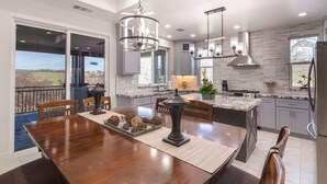A modern kitchen with a large island, pendant lighting, and a view of the outdoors.