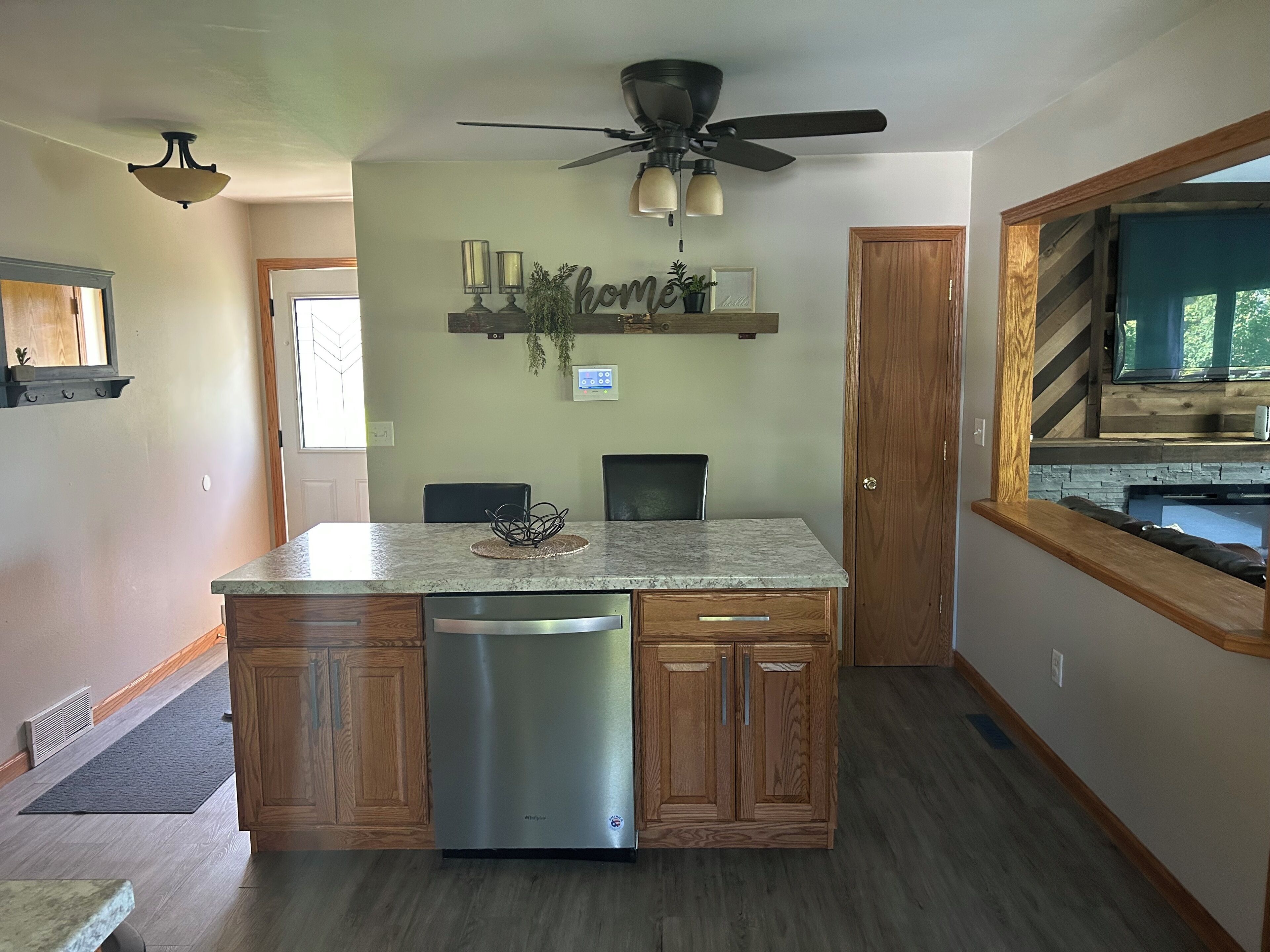 A kitchen with a central island, wooden cabinets, a dishwasher, a ceiling fan, and a built-in TV.