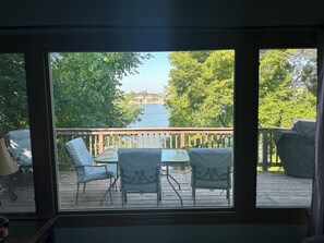 A view from inside a room to a deck with a table and chairs, overlooking a body of water and trees. - Serene Lakefront Escape With Stunning Views & Sunsets - Rice Lake, ND (Douglas)
