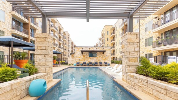 Une piscine entourée de bâtiments en pierre dotés de balcons, avec des chaises longues et des parasols à proximité.