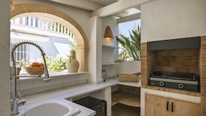 A compact kitchen with a sink, a built-in grill, and a window overlooking a garden.