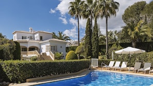 A swimming pool with lounge chairs and a white building with a tiled roof.