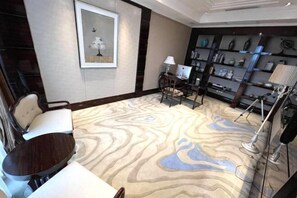 Hotelkamer met een groot, patroonrijk tapijt, een bureau met stoel, een boekenkast en een lijst met kunstwerk aan de muur.