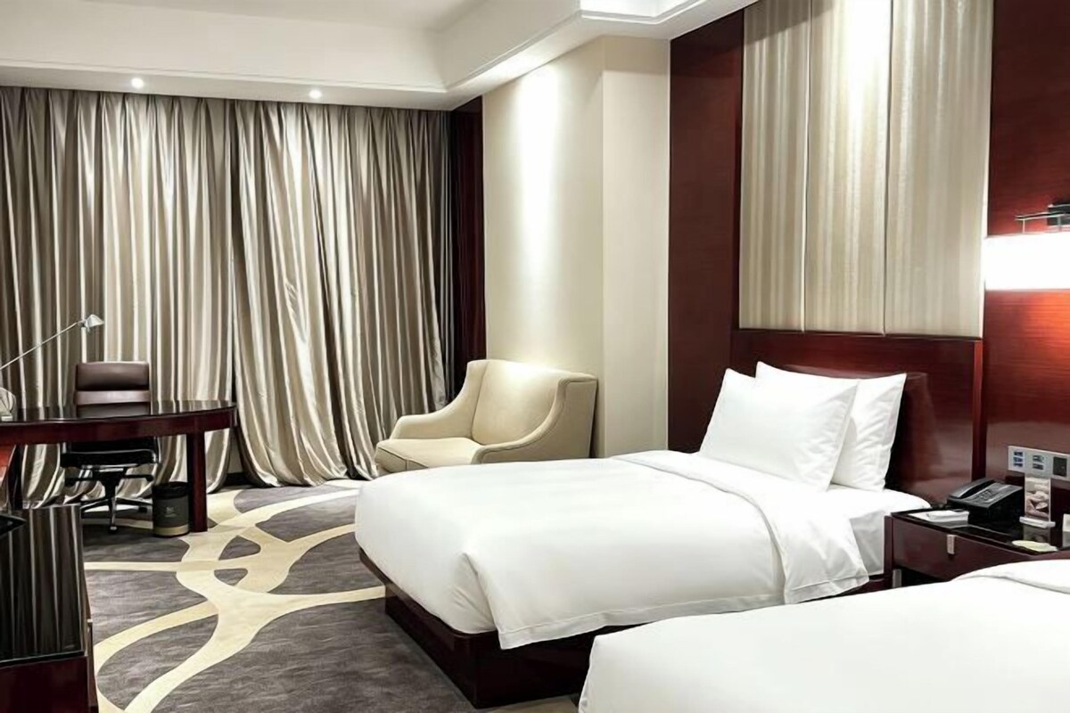A hotel room with a bed, a desk, a chair, and a large window with curtains.