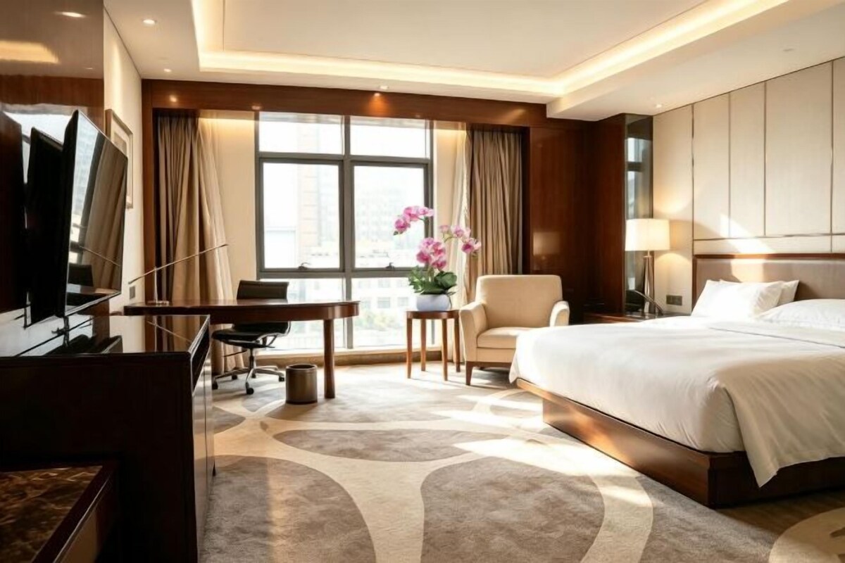 A hotel room with a bed, a desk, a chair, a television, and a window with curtains.