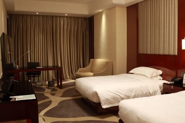 Hotelkamer met twee bedden, een bureau, een stoel, een televisie en een groot raam met gordijnen.