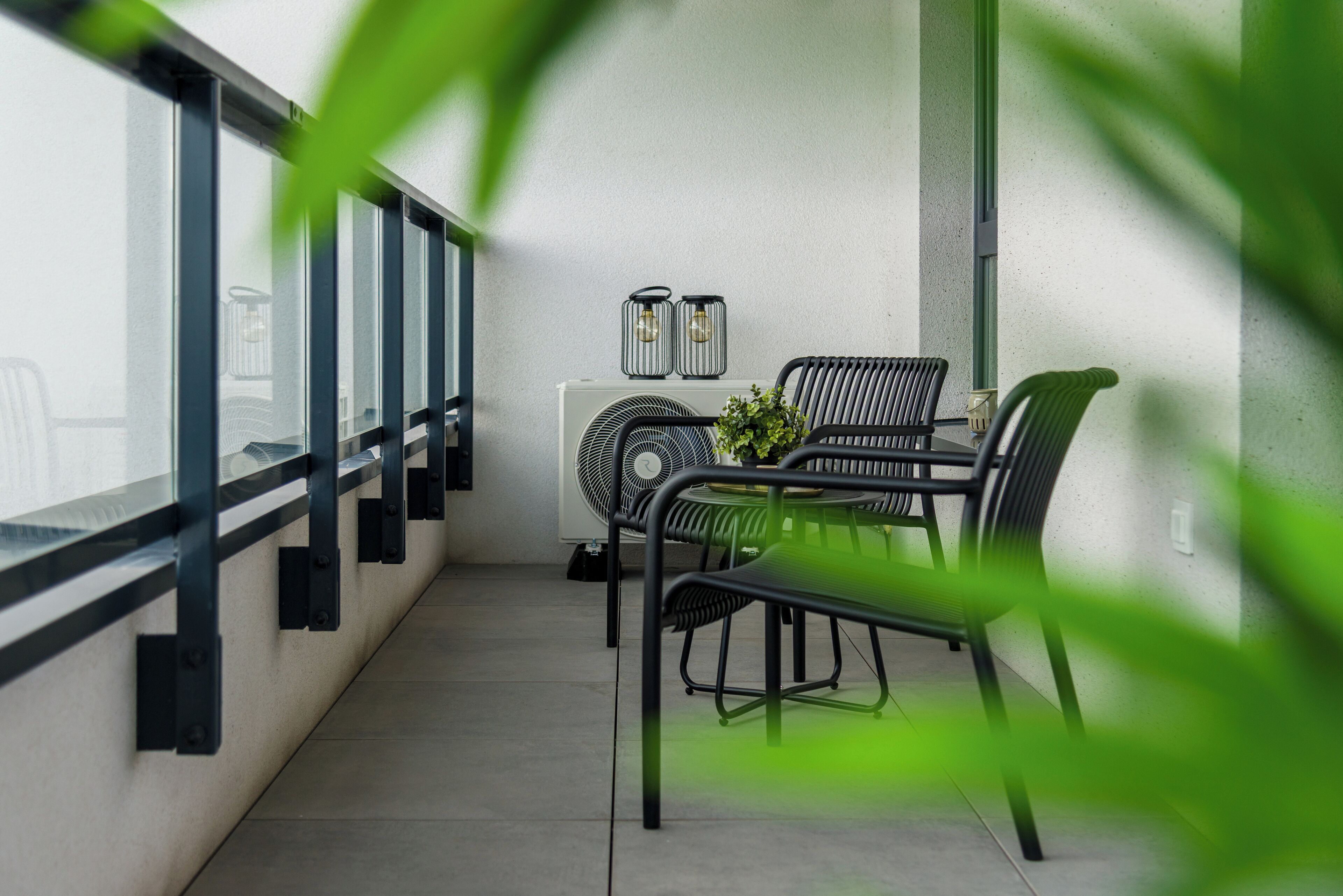 A balcony with a table and chairs, a fan, and two wall-mounted light fixtures.