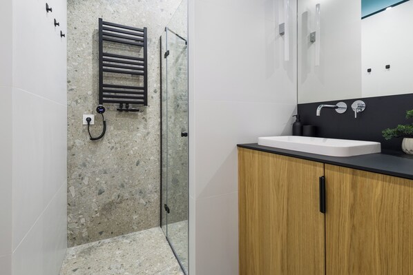 Un baño moderno con cabina de ducha de vidrio, un mueble de madera y un lavabo blanco.