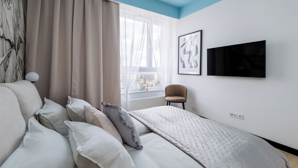 A modern bedroom with a bed, a chair, a TV, and a window with curtains. - Sky by Kairos Apartments (Katowice)