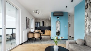 A modern living room with a sofa, a coffee table with a vase, and a dining area with chairs and a table. - Sky by Kairos Apartments (Katowice)