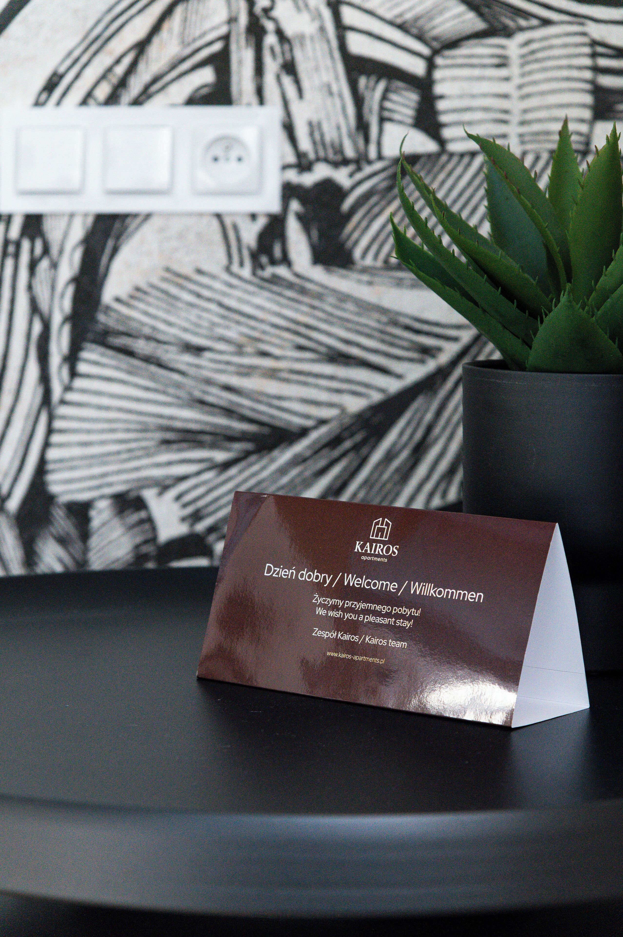 A business card on a table with a black and white abstract wall in the background and a potted plant.