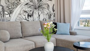 A modern living room with a beige sofa, a black coffee table, and a floral wall mural. - Sky by Kairos Apartments (Katowice)